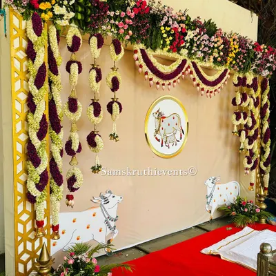 A beautiful and auspicious cow-themed backdrop for a traditional ceremony. The setup features hanging floral arrangements and illustrations of Kamadhenu, the sacred cow, symbolizing purity and prosperity.