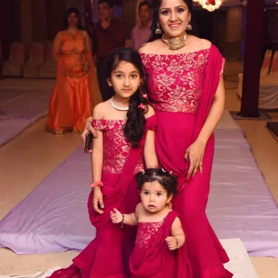 A happy family celebrating in their custom-made Aashirwad Boutique outfits. I designed these matching off-shoulder gowns in a vibrant magenta, with detailed embroidery on the bodice and a stylish draped saree effect.