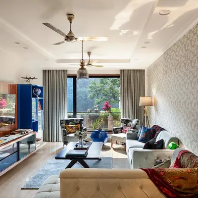 The living room at Ridge View, where botanical print wallpaper mirrors the greenery outside. We used soft blue sofas and curated lounging chairs to create a sanctuary for quiet moments, with a striking deep blue shelf housing books and memorabilia.