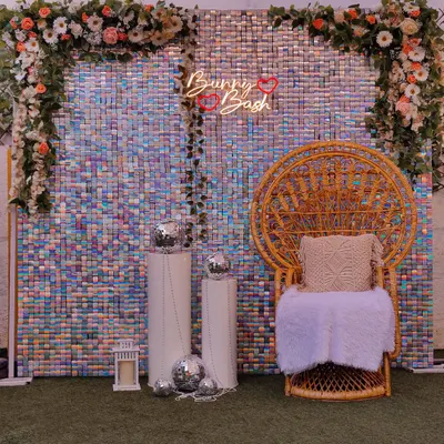 A glamorous sequin backdrop with a peacock chair. This iridescent wall is perfect for a baby shower, haldi, or mehendi, and can be customized with a neon sign and floral arrangements.