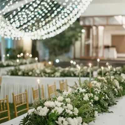 A vision in white. For this elegant cocktail dinner, we designed a stunning tablescape with a lush runner of white flowers and greenery, set under a transparent roof filled with fairy lights for a magical, starlit dining experience.