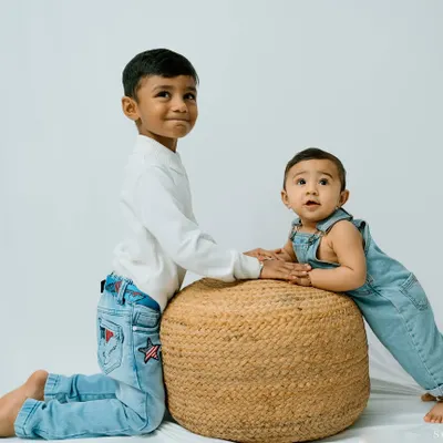 A classic studio portrait of two brothers. The older brother rests his hand gently on a stool where his baby brother is propped up, a sweet image of their budding friendship.