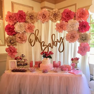 A classic "Oh Baby" shower theme with a beautiful dessert table. The backdrop features a curtain of paper flowers in shades of pink and gold, creating a sweet and celebratory setting.