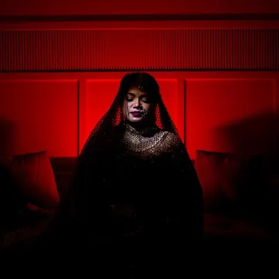 A moment of quiet reflection. This artistic bridal portrait uses deep red tones and shadows to create a sense of mystery and elegance, focusing on the bride's serene expression.