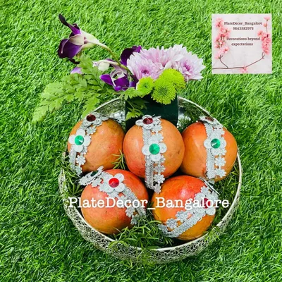 Pomegranates decorated with silver lace and kundan stones, arranged in a silver filigree bowl with fresh flowers. This is a classic and elegant fruit platter design.