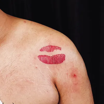 A vibrant red lipstick kiss tattoo on the shoulder. This is a fun, bold, and playful piece that makes a statement.