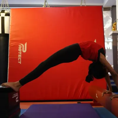 A student performs a deep backbend stretch, using training blocks and a low beam for support. We use various pieces of equipment to help young athletes safely deepen their flexibility.
