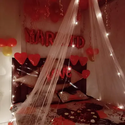 Welcome the newlyweds with a romantic first night decoration. This setup features a delicate canopy with fairy lights over the bed, "MARRIED" foil balloons, and red heart accents for a touch of romance.