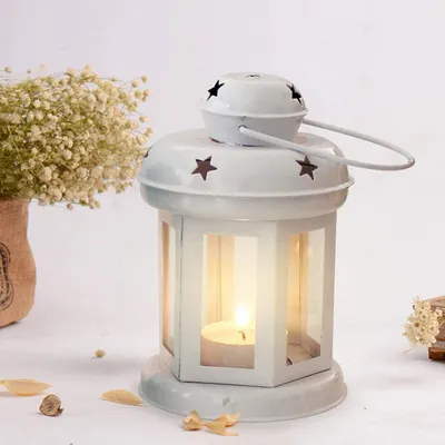 This white metal lantern is a charming holder for a single tealight candle. It protects the flame while casting a gentle, starry pattern of light, perfect for indoor or outdoor decor.