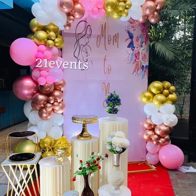 A classic 'Mom to Be' baby shower setup with a pink, rose gold, and white balloon arch. The fluted pedestals and floral accents add a touch of elegance.