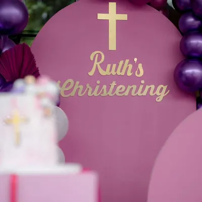 A beautiful Christening setup in a rich magenta. The gold lettering and cross on the arched backdrop create an elegant and celebratory feel for this sacred occasion.