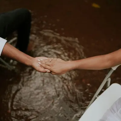 An artistic and symbolic shot of a couple holding hands while seated in chairs surrounded by water. This conceptual photo is about connection and trust.