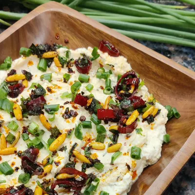 Our creamy Whipped Pinenut Feta dip, generously topped with sun-dried tomatoes, toasted pine nuts, and fresh spring onions. It's perfect with crackers or grilled vegetables.