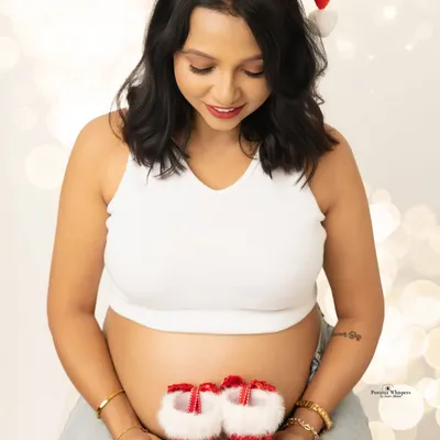 An expectant mother holds a tiny pair of festive booties, a sweet and hopeful portrait for her Christmas-themed maternity shoot. This is a wonderful way to announce and celebrate your growing family.
