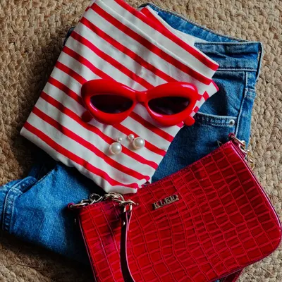 This flat lay captures a perfect Parisian-inspired summer look. The key is in the accessories: a red-hot bag, matching retro sunglasses, and classic pearl earrings elevate a simple striped top and jeans.