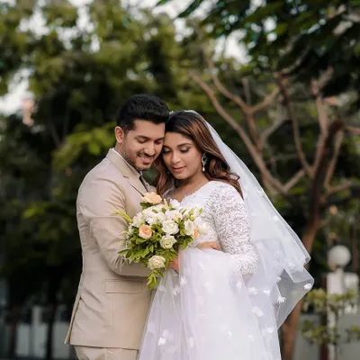 A gentle moment between a bride and groom after their Catholic wedding ceremony, captured outdoors. The bride's white gown and veil are beautifully highlighted.
