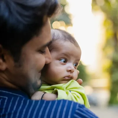 A heartwarming shot of a father holding his newborn baby over his shoulder. The baby's curious expression and the soft outdoor light make this a precious memory.