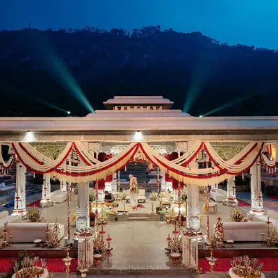 A stunning twilight view of a Kerala-inspired wedding mandap, with the mountains in the background and the structure adorned in traditional red, white, and green florals.