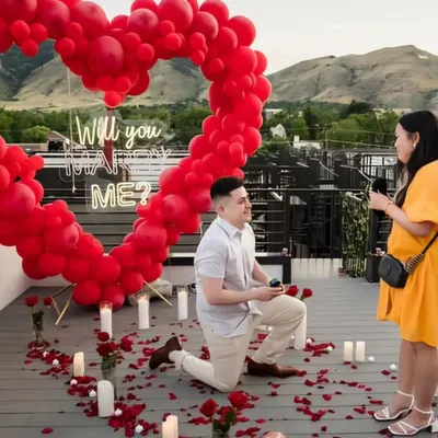 The perfect moment captured. We set the stage for a lifetime of memories with this rooftop proposal, featuring a giant red balloon heart, a "Will you marry me?" neon sign, and a romantic pathway of candles and rose petals.