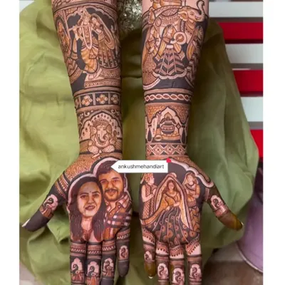 A truly personalized bridal mehandi featuring realistic portraits of the couple on one palm. The other hand and arms depict a full wedding story with Radha-Krishna, Lord Ganesha, and baraat procession elements.