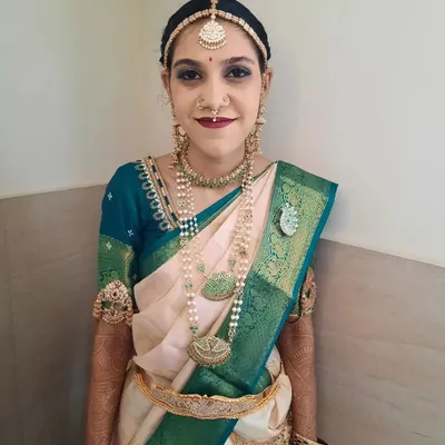 A full portrait of Bride Shalini for her Muhurtham. The makeup features a bold lip and striking eye makeup that beautifully complements her traditional off-white and green silk saree and antique-finish jewellery.