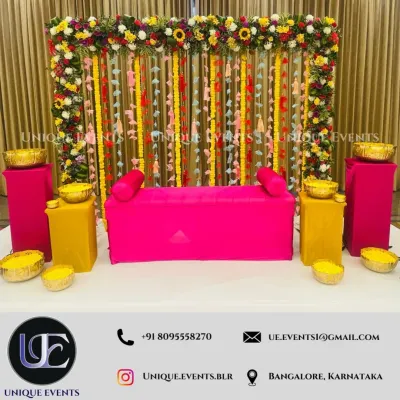 A complete Haldi ceremony setup designed for photos and fun. The bright pink seating, yellow accents, and a backdrop of marigolds and floral strings create a picture-perfect and energetic environment.