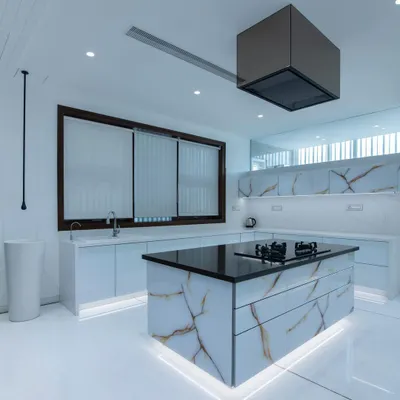 A stunning example of a modern minimalist kitchen, featuring a monolithic island wrapped in book-matched porcelain with gold veining. Under-cabinet and island lighting adds a floating effect to the clean, all-white design.
