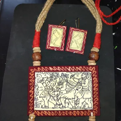 This rectangular pendant necklace is my tribute to the Kalighat and Jamini Roy style of painting. The piece depicts a festive scene with musicians, hand-drawn on a fabric base and framed in deep red. The set includes matching earrings, all crafted to be lightweight and culturally rich.