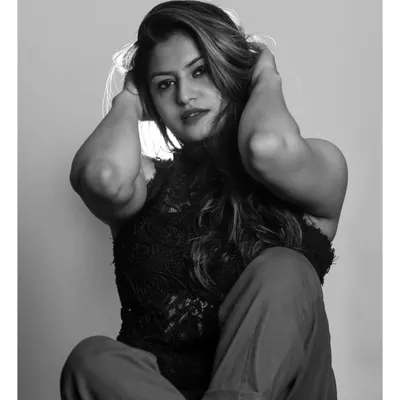 A powerful black and white studio portrait. The strong contrast and backlighting create a dramatic halo effect around the model's hair, while her pose conveys confidence and intensity.