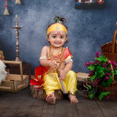 Our Little Krishna theme is a favorite for Janmashtami. This full setup shows the baby boy dressed as Krishna, sitting happily amongst traditional props like a pot, baskets, and marigold flowers.