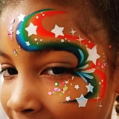 A close-up of a vibrant rainbow and stars design. This style of creative face painting wraps around the eye, making the guest feel truly special and ready to celebrate.