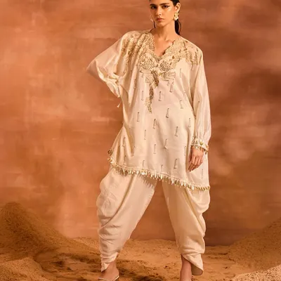 The Orion Kaftan Set in a classic ivory. This ensemble features a stunningly embellished kaftan with phoenix-inspired motifs and pearl tassels, paired with comfortable and stylish solid dhoti pants.