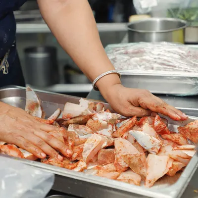 There is nothing better than using bare hands to create, enhance, and elevate a dish. Here, I am marinating fresh fish, ensuring every piece is coated with our special masala mix. This hands-on approach is the essence of our homestyle cooking.