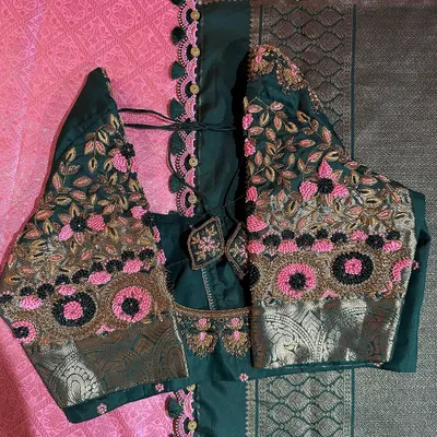 This is a close-up of a dark green blouse we designed to pair with a pink saree. It features beautiful floral embroidery using pink, gold, and black threads, with unique circular motifs that add a modern touch.