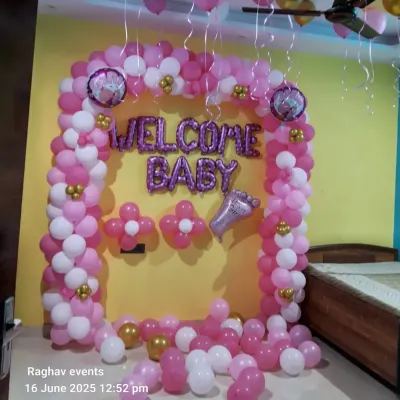A classic "Welcome Baby" decoration for a girl. This setup includes a pink and white balloon arch, "WELCOME BABY" foil letters, and small gold balloon accents.