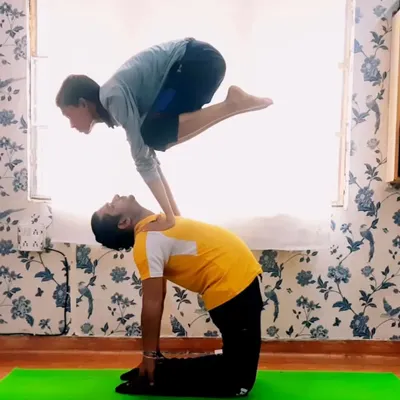This dynamic acro yoga pose combines the Camel Pose (Ustrasana) and Crane Pose (Bakasana). It requires immense core strength from the top person and a stable base from the partner, showcasing incredible balance and control.