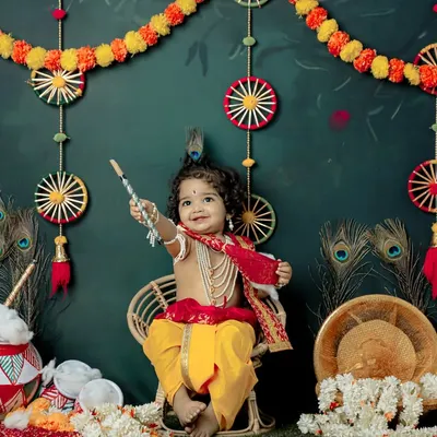 A joyful little Krishna celebrating Janmashtami in our studio. The vibrant backdrop with peacock feathers and marigolds creates a festive atmosphere for this divine photoshoot.