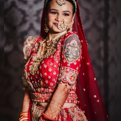 A radiant bride on her wedding day. This look features a traditional red lehenga with intricate embroidery, paired with a statement nath and matha patti for a truly royal feel.