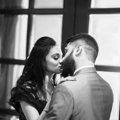 An intimate black and white portrait, capturing a kiss against a beautifully lit window. Monochrome enhances the romance and timelessness of the moment.