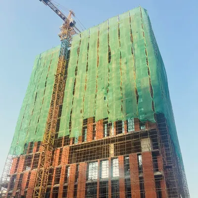 An office tower under construction, with its brick facade taking shape beneath the scaffolding. The green safety netting creates an unintentional, large-scale art installation, reminiscent of the work of Christo and Jeanne-Claude.