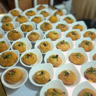 A display of a classic Indian sweet, perfectly portioned in individual white bowls and garnished with chopped nuts and rose petals. This presentation makes it easy for guests to enjoy at a large event.