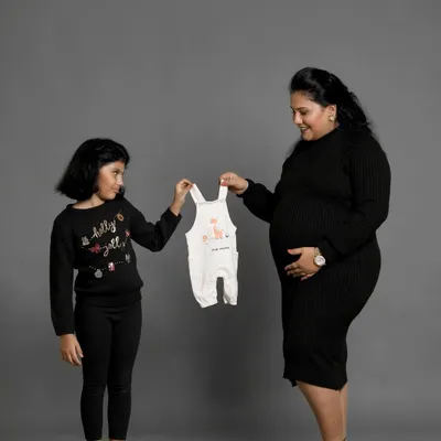 A sweet moment between a mother and daughter, looking forward to the new baby's arrival. Using a tiny baby outfit as a prop is a lovely way to announce the new addition to the family.