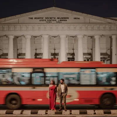 A classic Mumbai moment. The iconic red BEST bus adds a dynamic blur of color to this romantic shot in front of the Asiatic Society Library, creating a truly cinematic pre-wedding photograph.