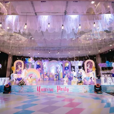 A full shot of the magical unicorn-themed birthday party we produced. The setup included a custom-designed stage with unicorn and rainbow cutouts, multiple balloon arches, a carousel prop, and a pastel-colored dance floor.