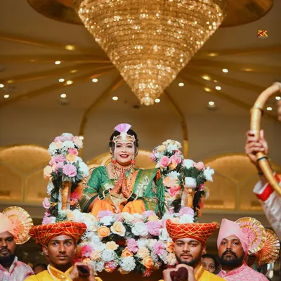 A grand doli entrance for the Maharashtrian bride. Seated in a beautifully decorated palanquin and surrounded by family, she makes her way to the ceremony under a stunning crystal chandelier.