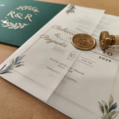 This bespoke wedding invitation features a printed vellum jacket, delicately wrapped and sealed with a luxurious gold wax seal. Paired with a deep glass glow green envelope, it's a perfect blend of timeless charm and contemporary style.