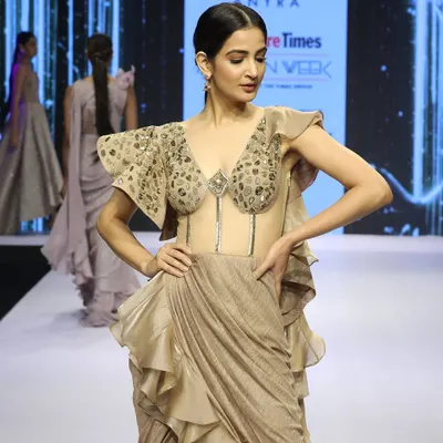 This draped saree gown, featured at Bangalore Times Fashion Week, is a showstopper. It has a transparent corset bodice with western-style embroidery and dramatic ruffles on the shoulder and hip, blending tradition with avant-garde design.