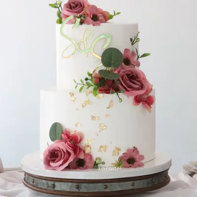 A classic two-tier engagement cake with a beautiful arrangement of dusty pink roses and eucalyptus leaves. The gold leaf flecks and iridescent initial topper add a touch of modern sparkle.