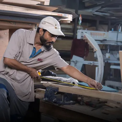 Behind every masterpiece are the hands of our skilled artisans. Here, one of our craftsmen meticulously measures and shapes a piece of wood, blending tradition with artistry. This dedication to handcrafted excellence is what breathes life into our luxury furniture.