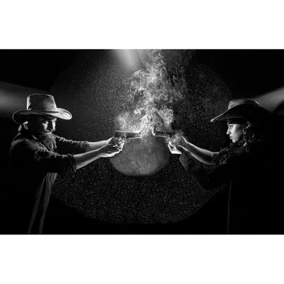 A conceptual photograph titled 'Flaming Guns at Shootout'. This staged, high-contrast black and white image uses dramatic lighting and captured motion to create a cinematic and confrontational scene.